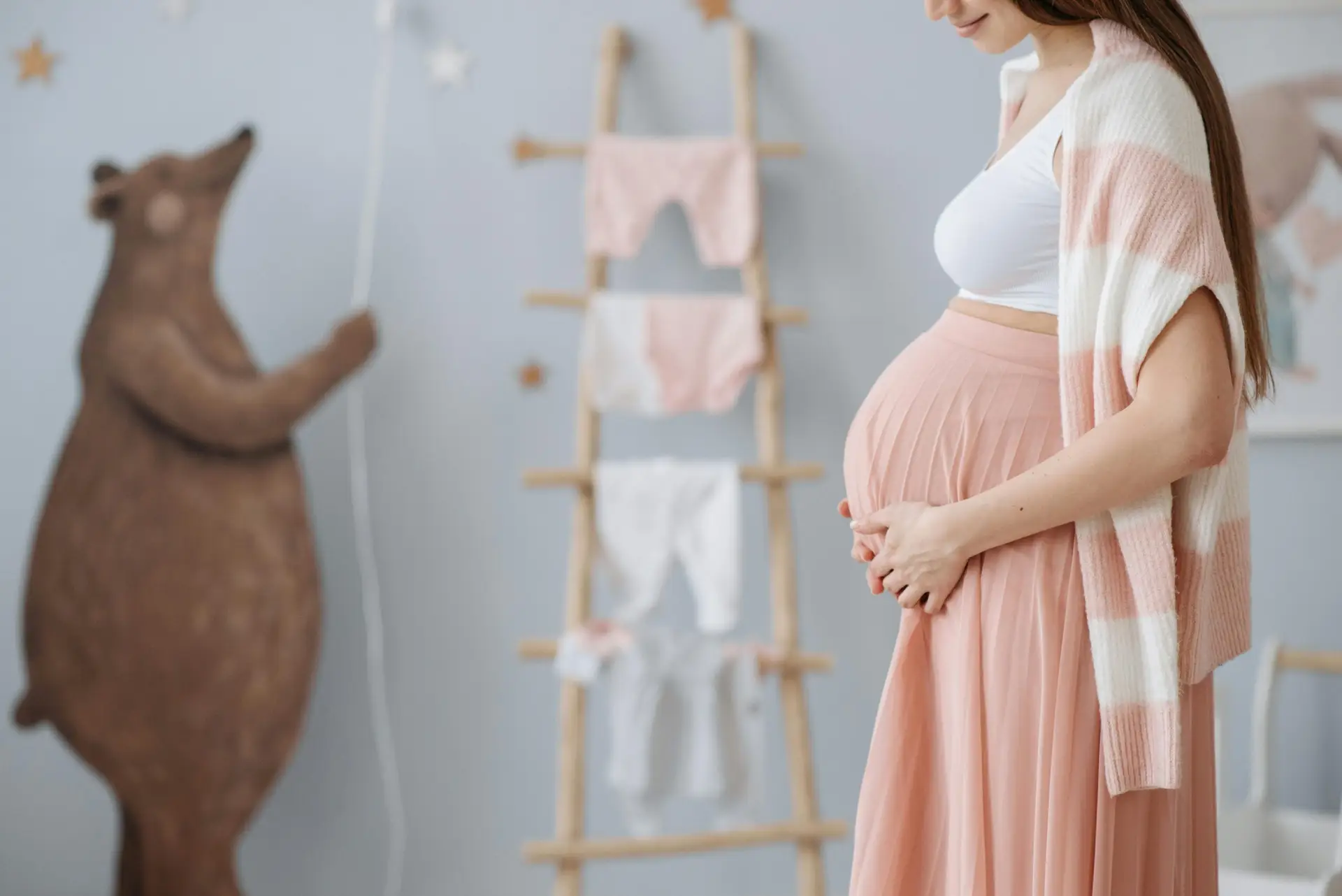 An expectant mother resting her hands on her belly in a calm nursery