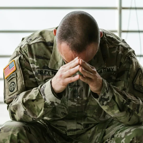 A soldier in camouflage sitting indoors, appearing stressed and overwhelmed.